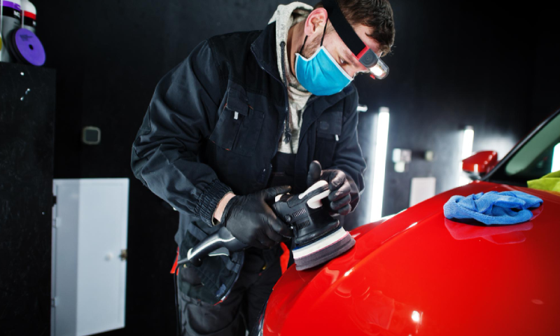 Car detailing concept Man in face mask with orbital polisher in repair shop polishing orange suv car Car detailing concept Man in face mask with orbital polisher in repair shop polishing orange suv car<br />